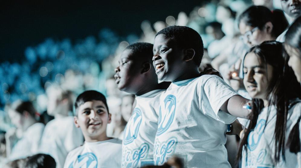 A group of children smile with their arms around each other.