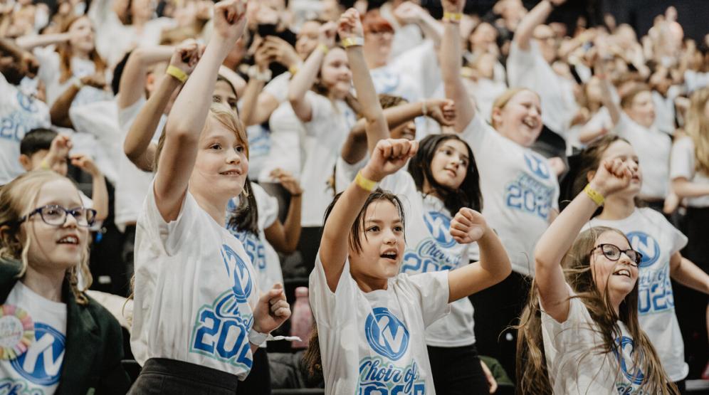 A group of children sing with their arms raised.